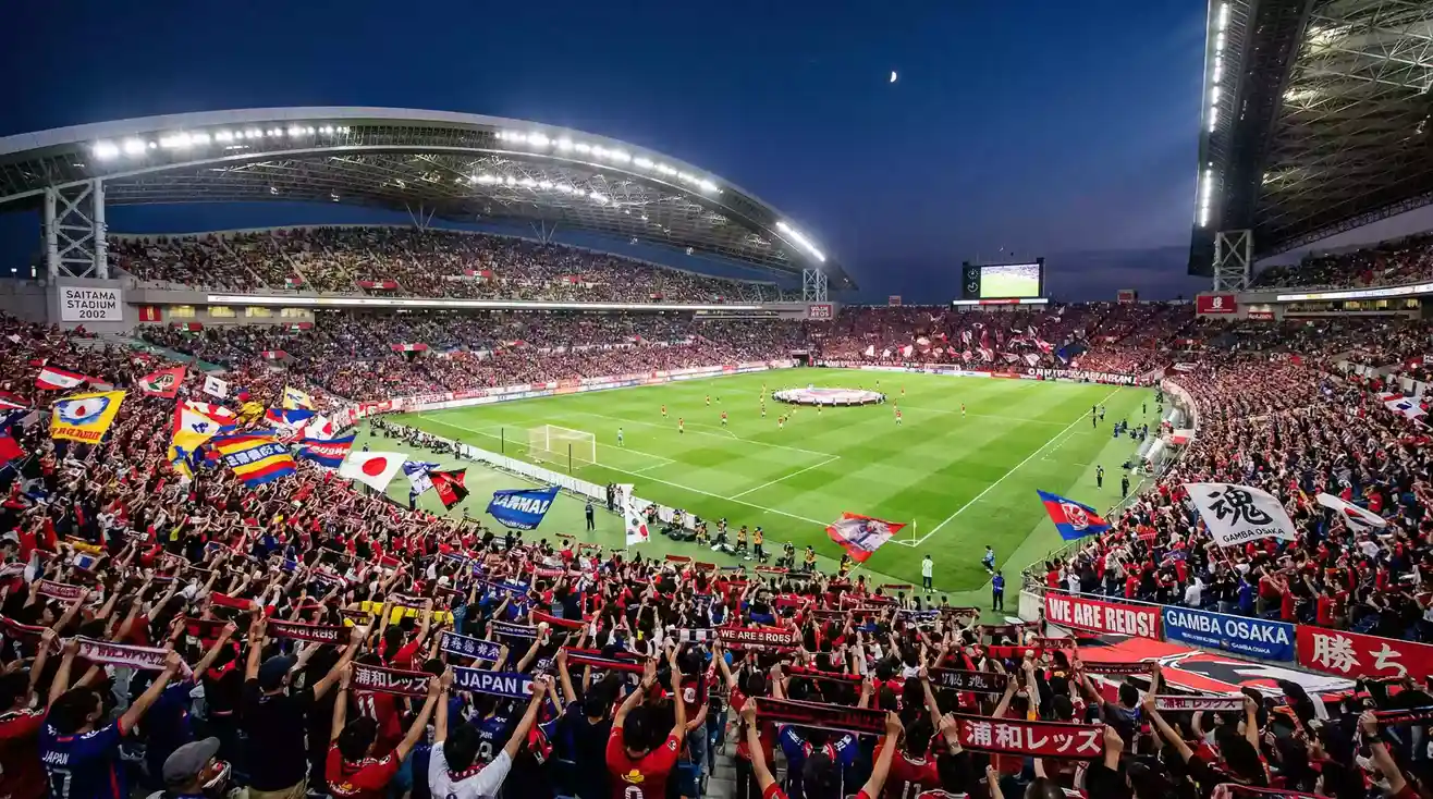 Estadio de fútbol japonés lleno de espectadores con banderas y bufandas de colores del equipo local