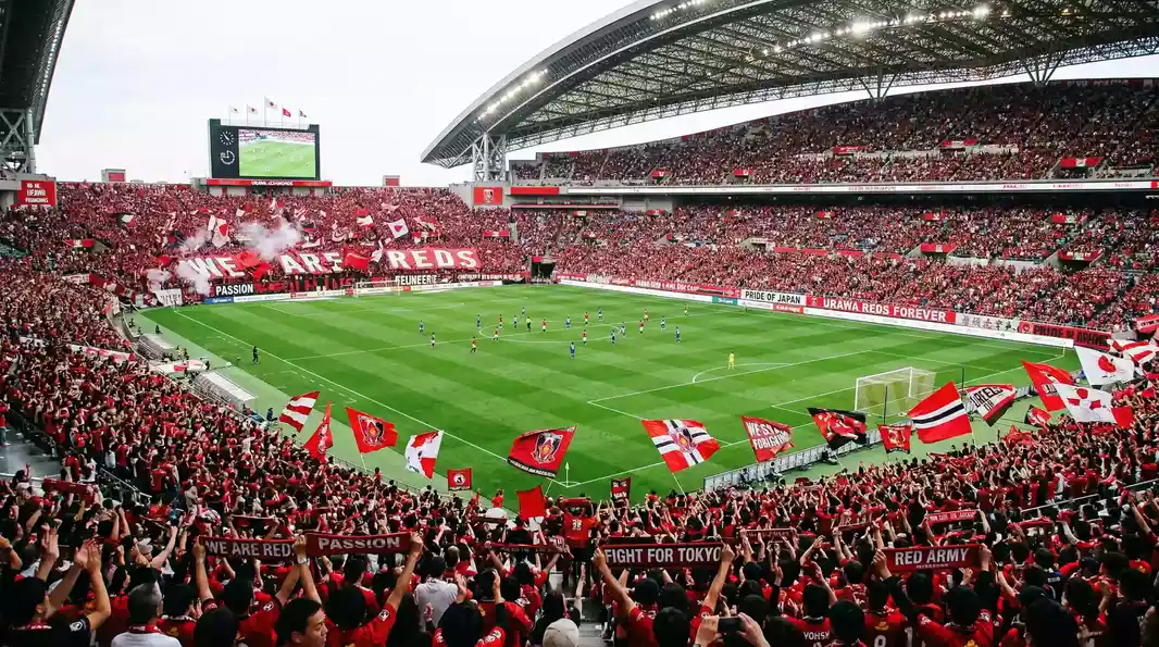 Estadio de Saitama lleno de aficionados de Urawa Red Diamonds con banderas rojas durante un partido de la J-League