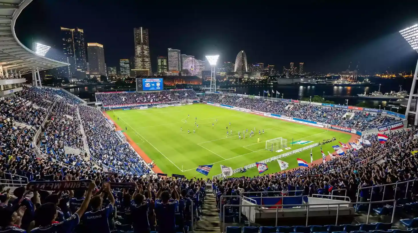 Estadio de Yokohama con el campo de fútbol iluminado y aficionados en las tribunas